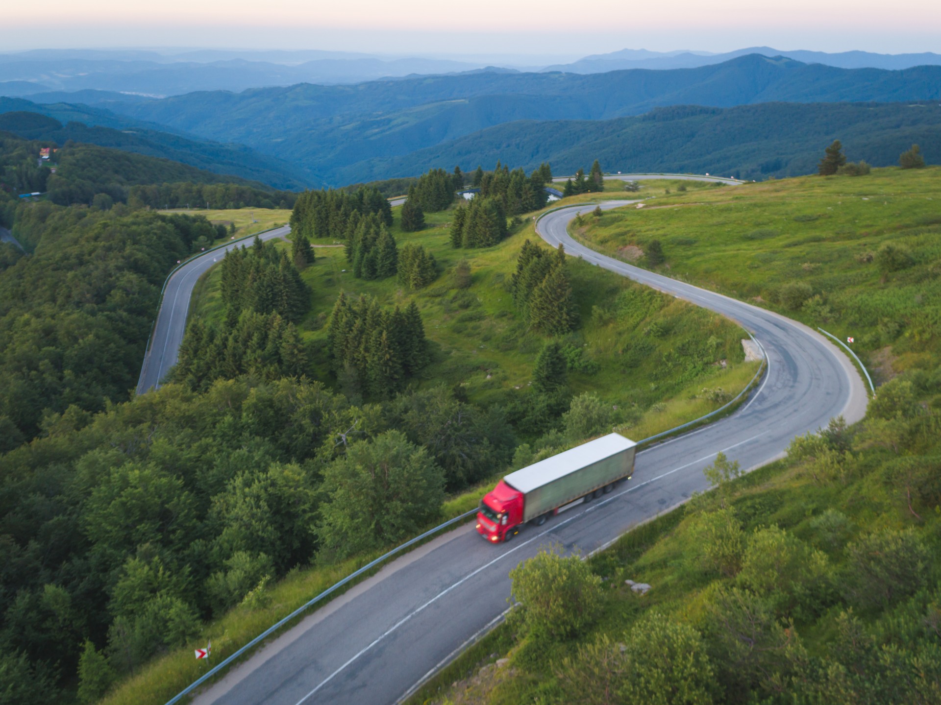 camion de livraison avec la cargaison conduit sur la route de forêt dans les montagnes au coucher du soleil.